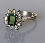 An 18ct white gold emerald and diamond cluster ring in a claw setting