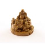 NETSUKE BUDAI AUF EINEM SHISHI, Mamut, auf einer ovalen Sockelplatte ein liegender großer Löwe auf