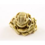 NETSUKE KABUTO MIT PFLAUMENZWEIGEN, der Helm mit einem Geweih und Befederung liegt auf einem Fächer