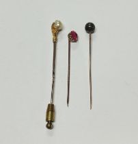 Three unmarked gold metall tie-pins, one a pink sapphire, one a claw surrounding mother of pearl and