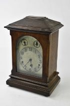 A late 19th/early 20th century German stained pine cased mantel clock, the decorated silvered dial