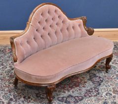 A Victorian carved walnut button back upholstered settee in pink material, on front scrolling legs.