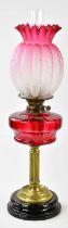 A Victorian oil lamp, the cranberry and clear fluted glass shade with wavy rim above the cranberry