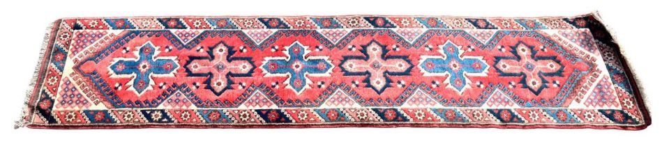 An antique Turkish runner with stylised motifs on a red ground, 280 x 70cm.