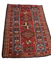 A Caucasian hand woven rug, worked with geometric designs against a red and blue ground, 238 x