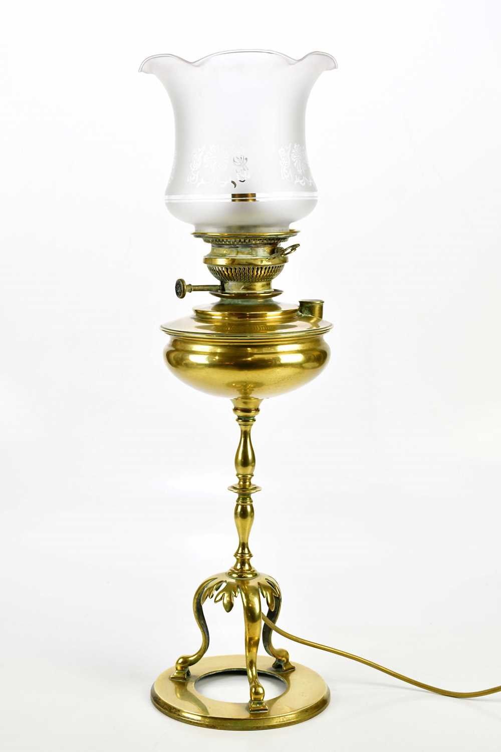 An early 20th century brass oil lamp with replacement frosted glass shade, on three scrolling
