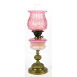 An early 20th century oil lamp with cranberry glass shade above cranberry and milk glass resevoir