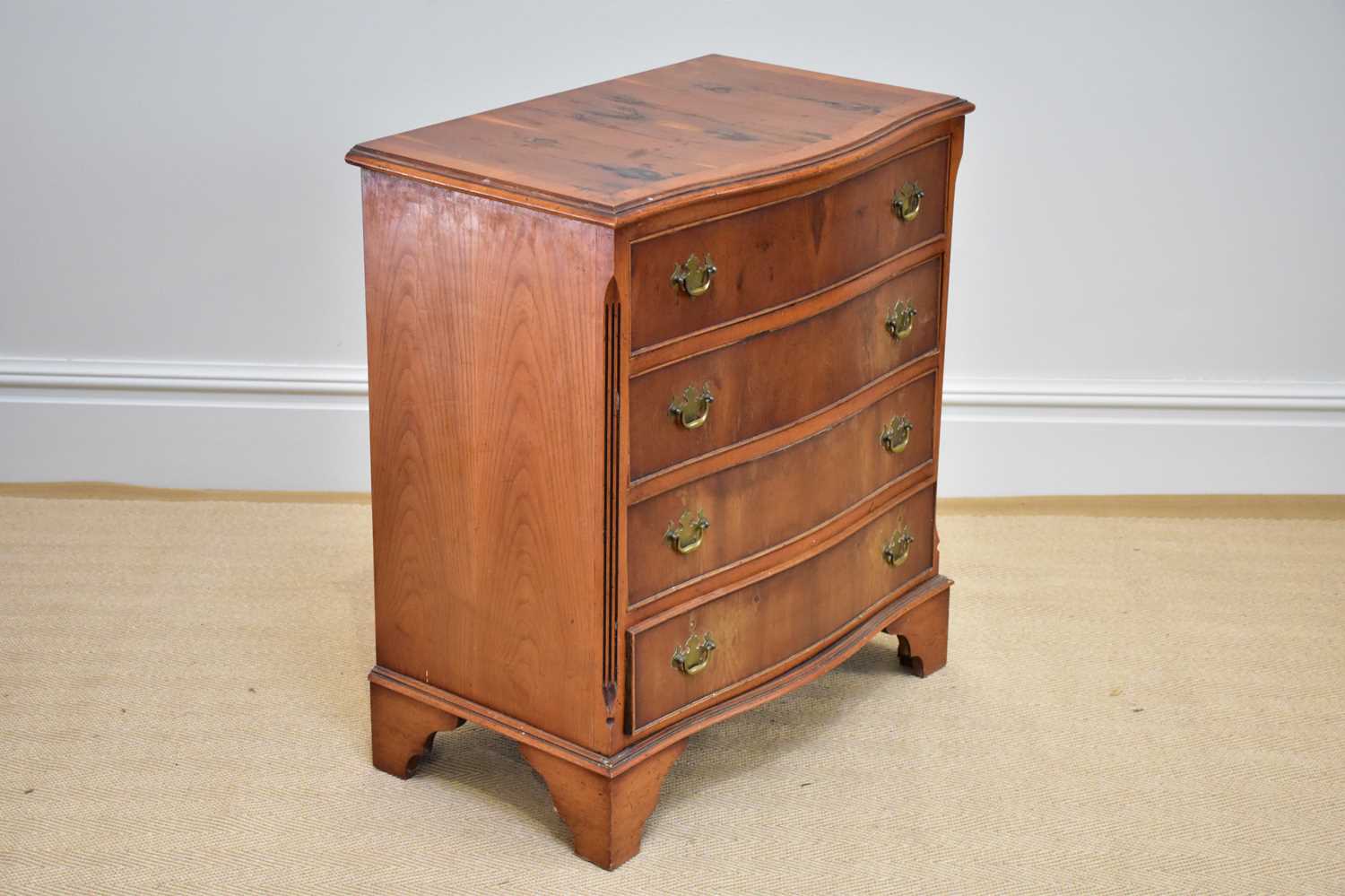 A reproduction serpentine fronted yew wood four drawer chest on bracket feet, width 72cm, depth