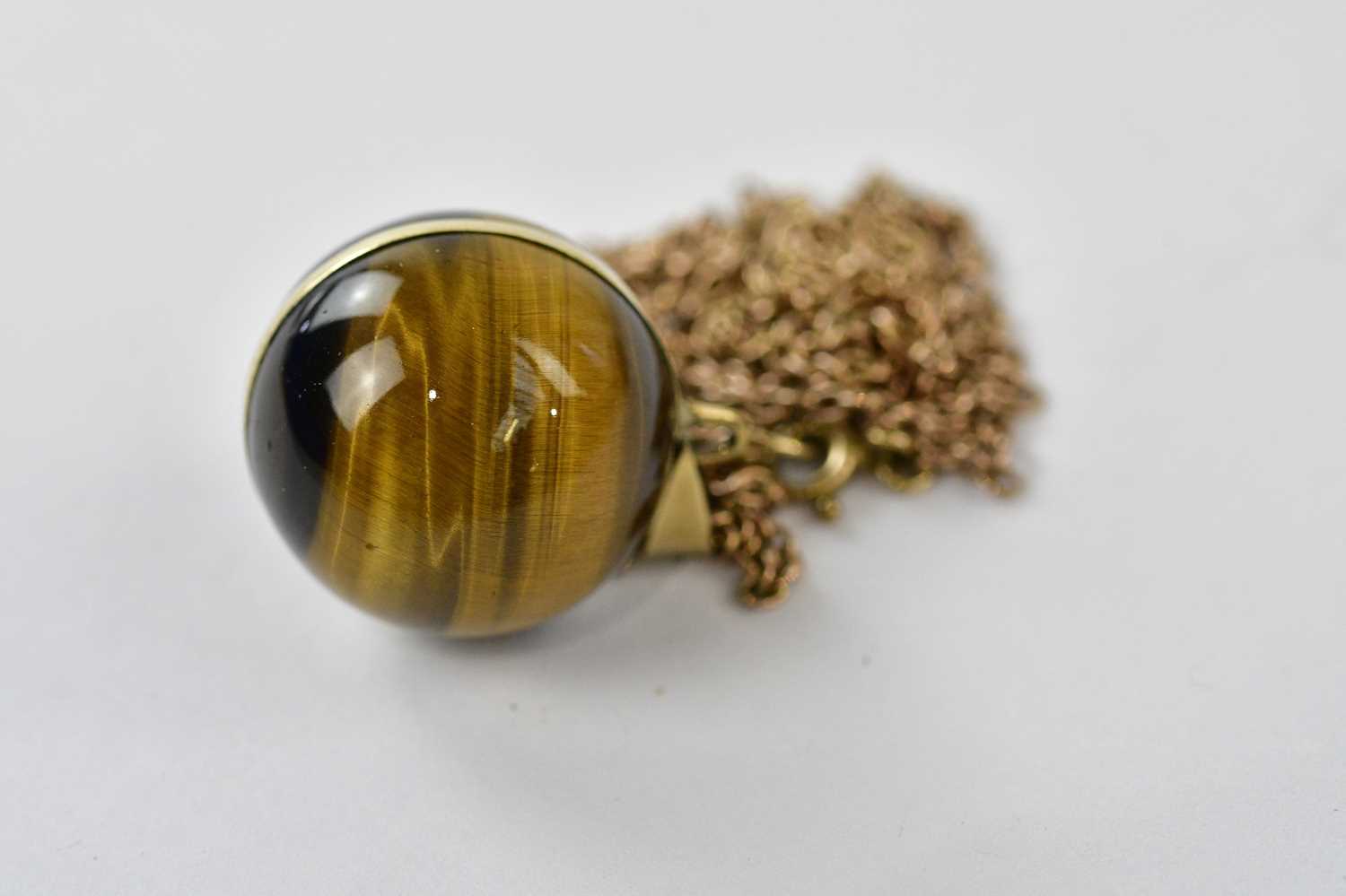 A yellow metal mounted tiger's eye pendant stamped 375, suspended on a chain.