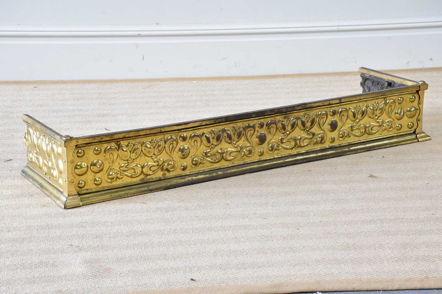 An Art Nouveau brass fender with embossed scrolling and floral decoration, length 129cm.