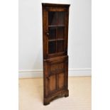 A reproduction oak freestanding corner cupboard, with moulded cornice above the glazed door and