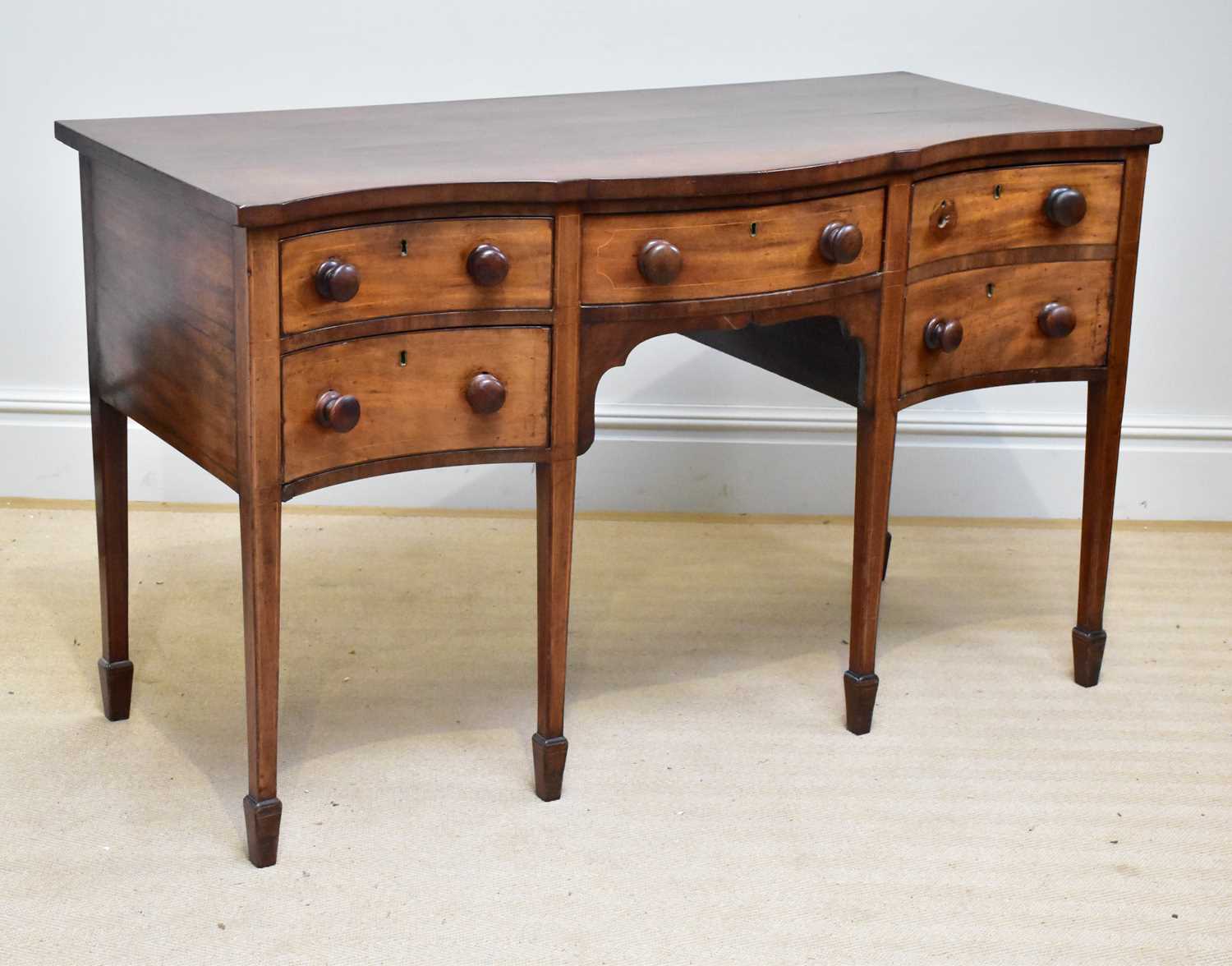 A late George III serpentine mahogany sideboard with three short drawers and one deep drawer on