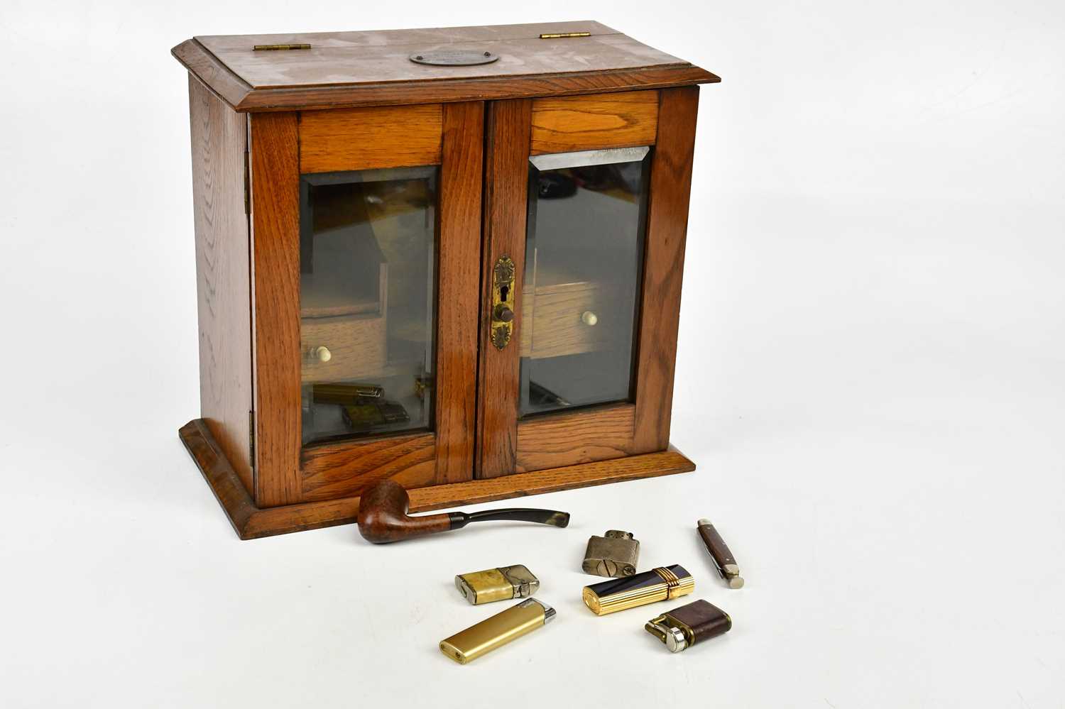 A 1920s oak smoker's cabinet with two glazed doors and a presentation plaque, five cigarette