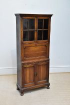 A 1920s oak bureau cabinet, with a pair of glazed doors above fall front and two panelled cupboard