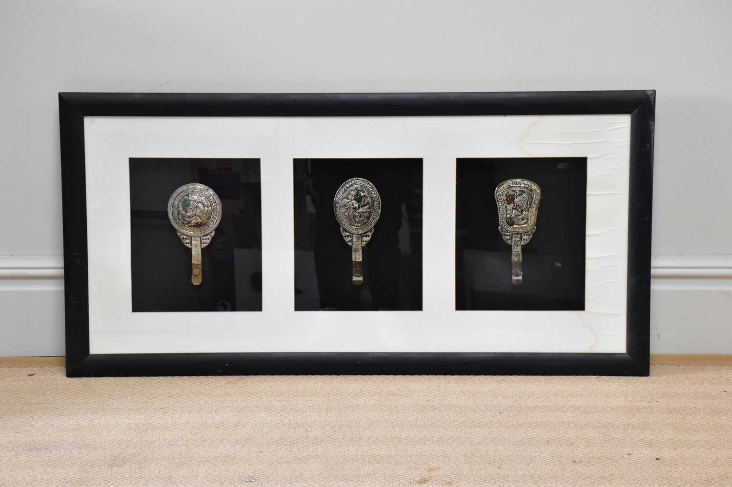 Three white metal Tibetan hand mirrors, framed and glazed, 58 x 119cm.