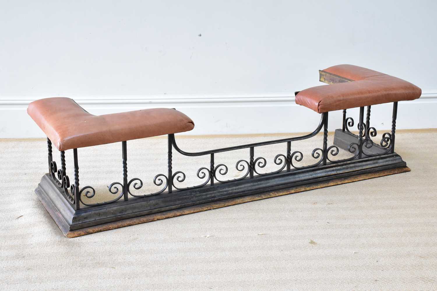 A wrought iron club fender with scrolling decoration and leather top, length 153cm.