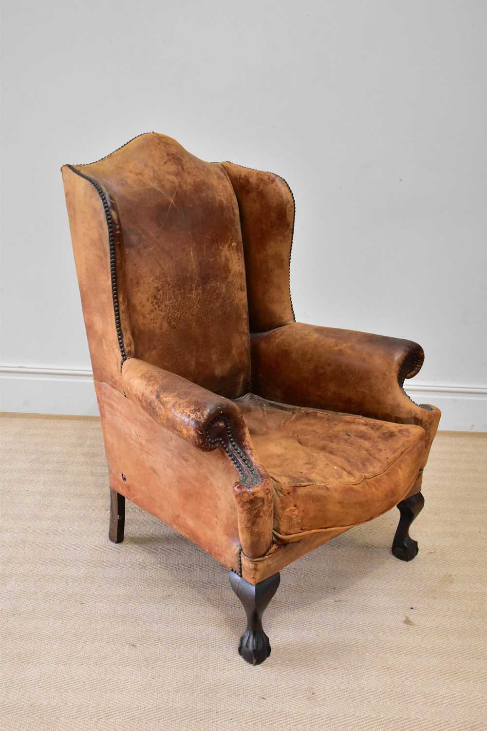 An early 20th century wingback armchair upholstered in a studded leather material, on ball and