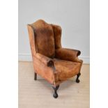 An early 20th century wingback armchair upholstered in a studded leather material, on ball and