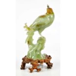 A Chinese carved jade figure of a bird perched upon a rock, sold with shaped wooden base, height