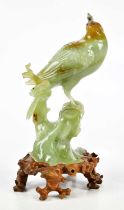 A Chinese carved jade figure of a bird perched upon a rock, sold with shaped wooden base, height