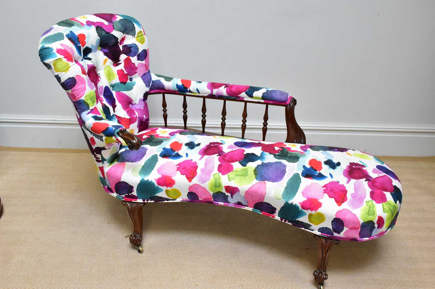 A Victorian rosewood framed chaise longue with spindle back and scrolling legs, upholstered in a