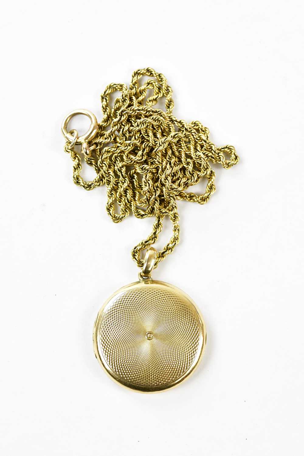 A 15ct yellow gold locket with engine turned decoration suspended on a yellow metal rope link chain,