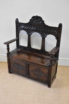 An early 20th century carved oak hall settle, with raised back and hinged seat, width 107cm,