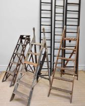 A collection of vintage wooden folding and step ladders.