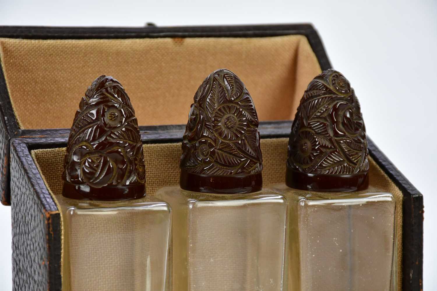 A cased set of three 1920s perfume bottles with carved resin lids, height 17cm. - Image 2 of 3