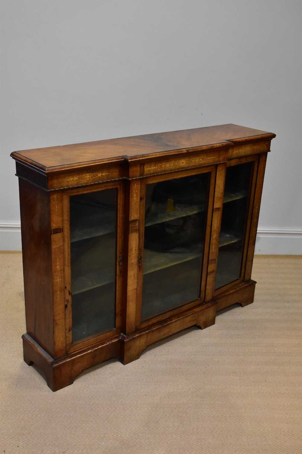 A Victorian breakfront walnut credenza, with three glazed doors enclosing shelves, on bracket