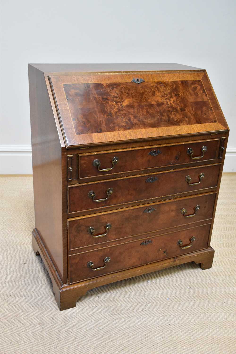 A reproduction walnut bureau, the fall front enclosing fitted interior above four drawers, on