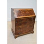 A reproduction walnut bureau, the fall front enclosing fitted interior above four drawers, on