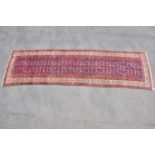 A red ground wool runner with geometric central pattern, 3390cm x 115cm. Condition Report: Colours