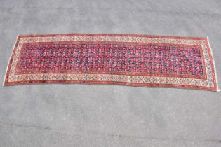 A red ground wool runner with geometric central pattern, 3390cm x 115cm. Condition Report: Colours