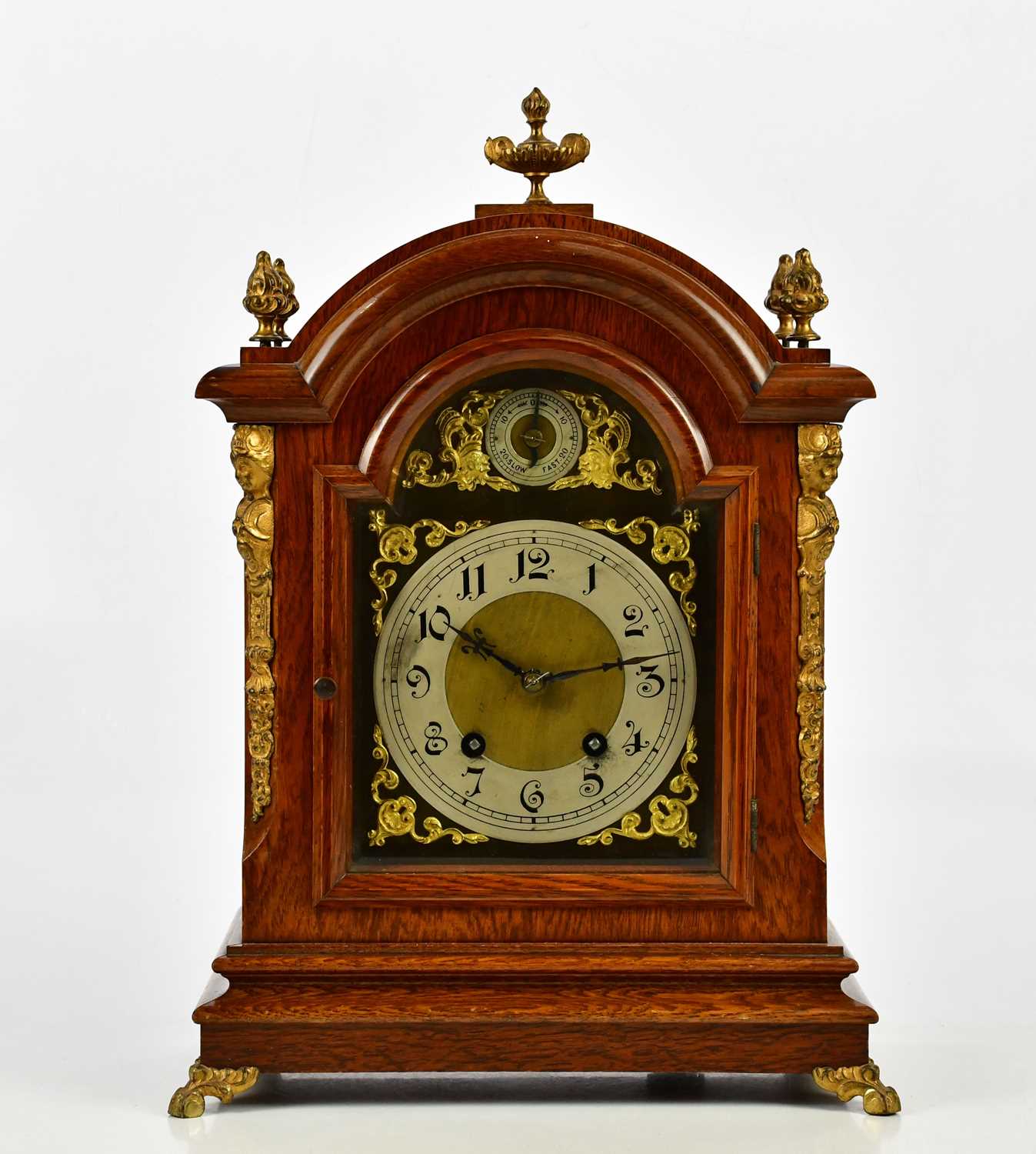 An early 20th century oak mantel clock with applied brass urn finial and four further scrolling