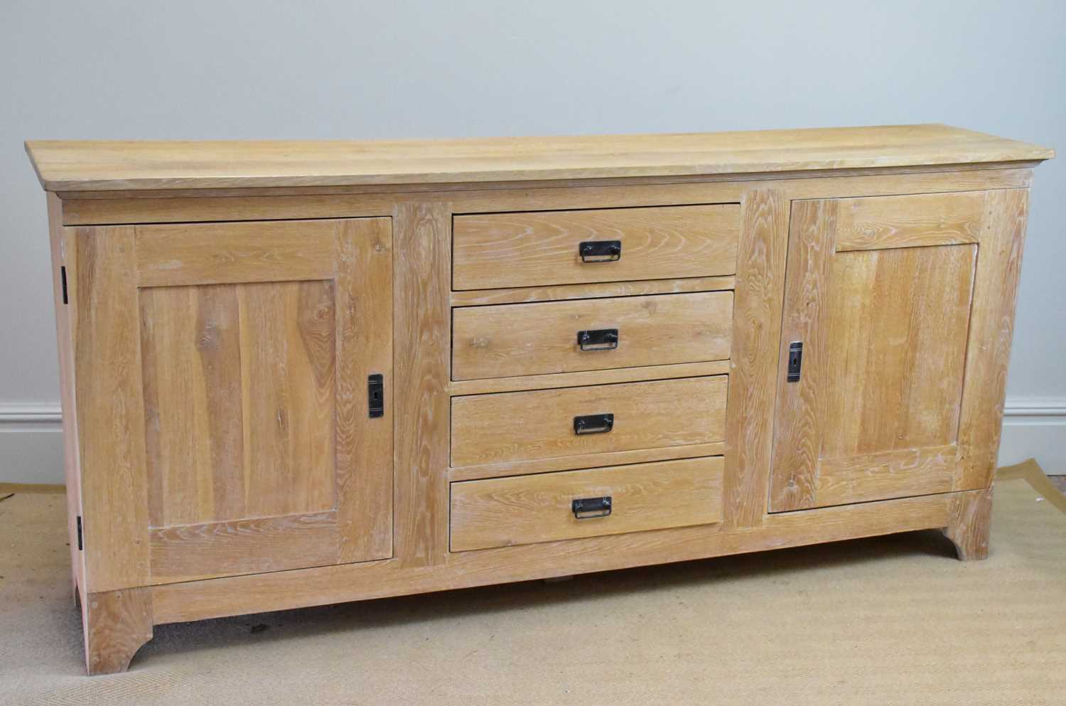 A modern limed oak sideboard with four drawers flanked by panelled cupboard doors, length 216cm,