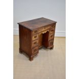 A George III mahogany kneehole desk with an arrangement of seven drawers and cupboard door, on