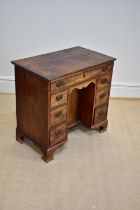 A George III mahogany kneehole desk with an arrangement of seven drawers and cupboard door, on