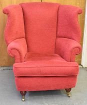 A good reproduction red upholstered wing armchair on turned supports with castors.