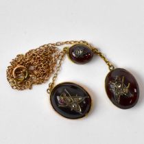 An Edwardian yellow metal necklace suspending three red hardstone pendants, decorated with small