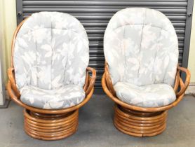A pair of modern revolving bamboo conservatory armchairs, with padded floral upholstered seats.