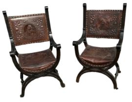 A pair of early 20th century leather embossed and ebonised framed X-frame elbow chairs.