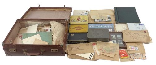 A quantity of all word stamps in bags and in tins, contained in a suitcase.