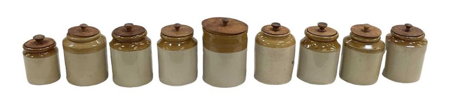 A collection of nine stoneware jars with wooden covers.