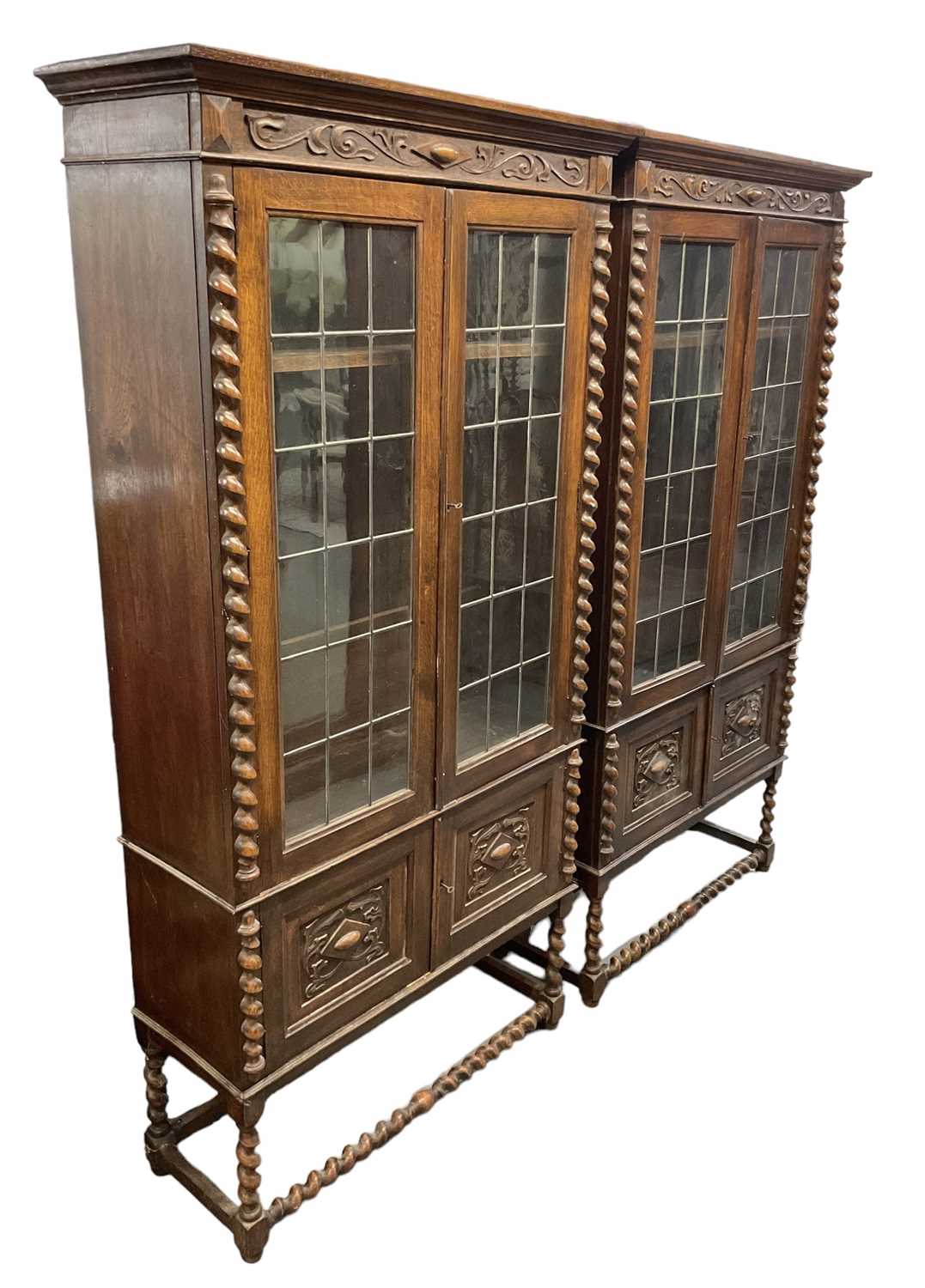 A pair of 1920s carved oak display cabinets on barley twist supports, height 190cm, width 96cm.