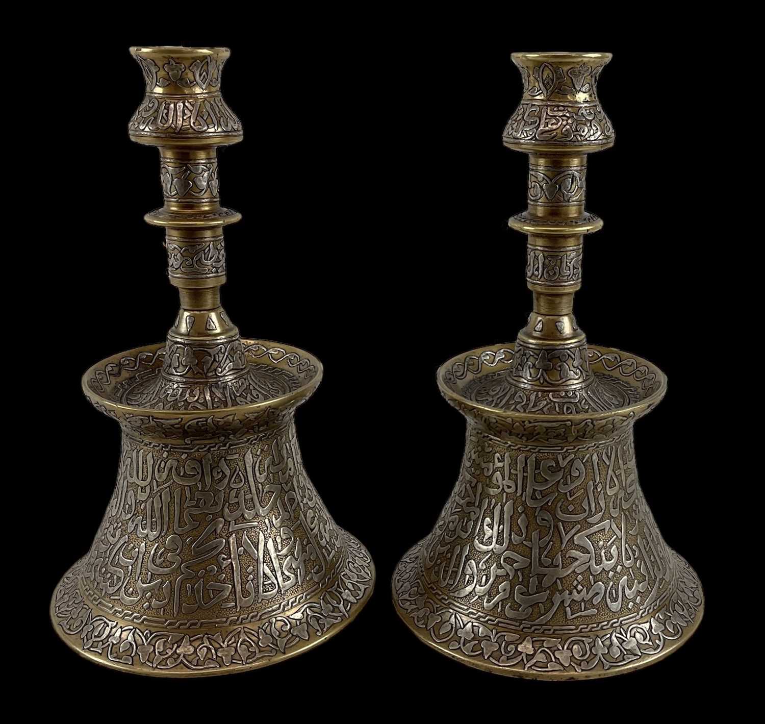 A pair of Islamic brass and silver inlaid candlesticks with Arabic calligraphy, height 30cm.