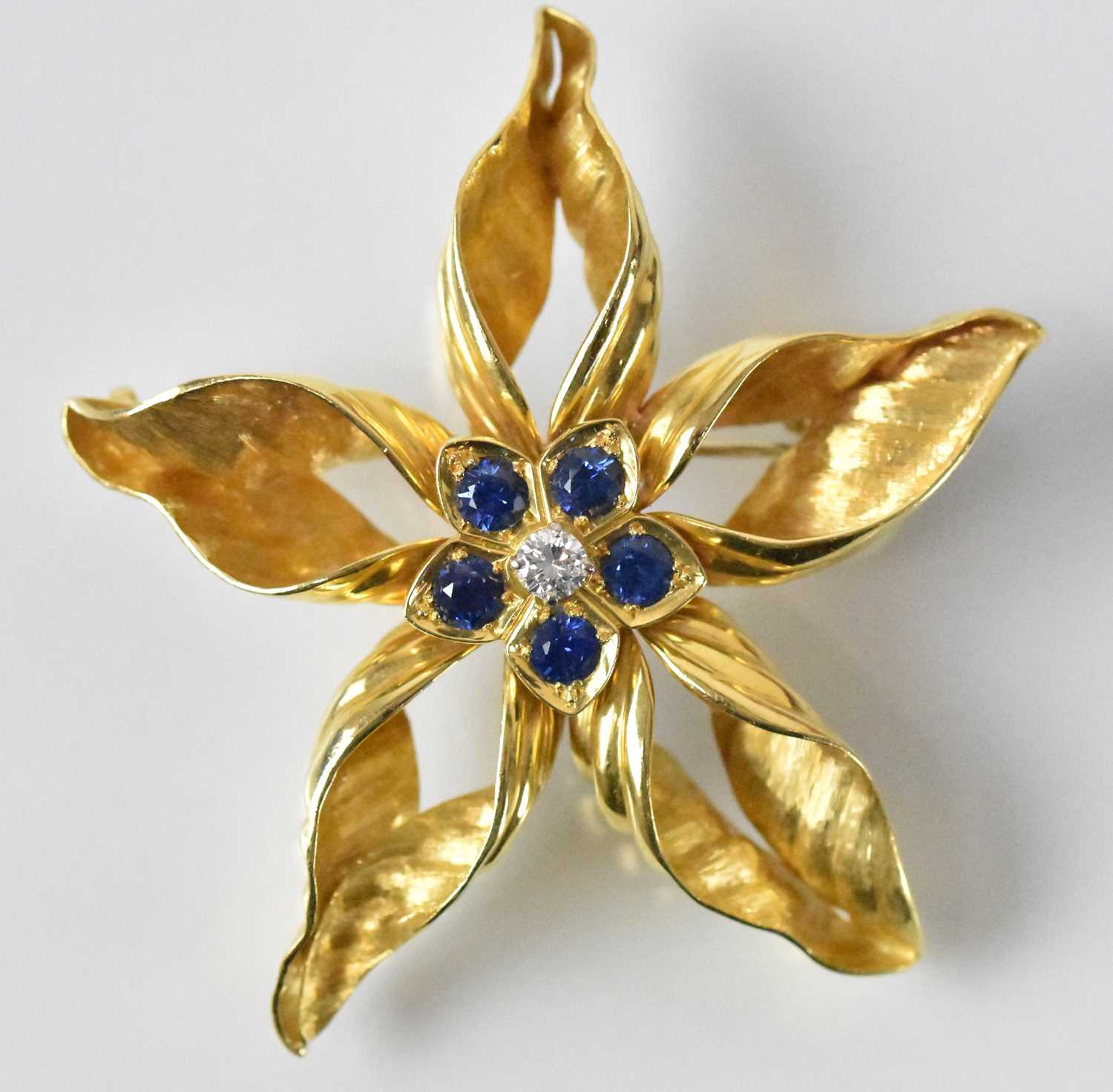 An 18ct yellow gold diamond and sapphire set flower brooch, the central stone approx 0.2ct,