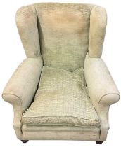 An early 20th century green upholstered wing armchair, raised on turned supports.