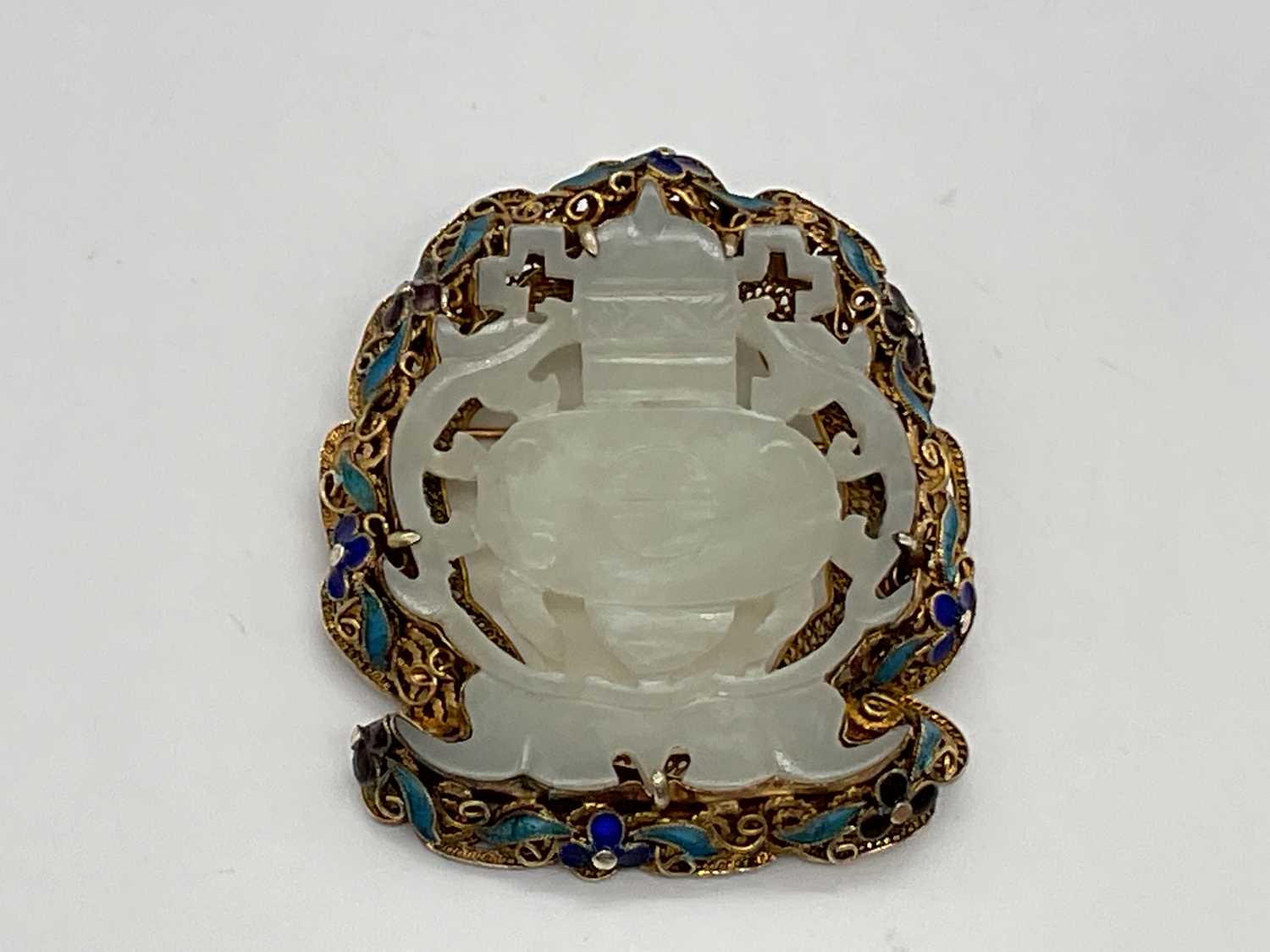 A Chinese pale jade plaque brooch in silver gilt and enamelled frame, 52 x 45mm.