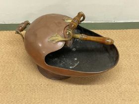 A Victorian copper coal scuttle with wooden handles and scoop.